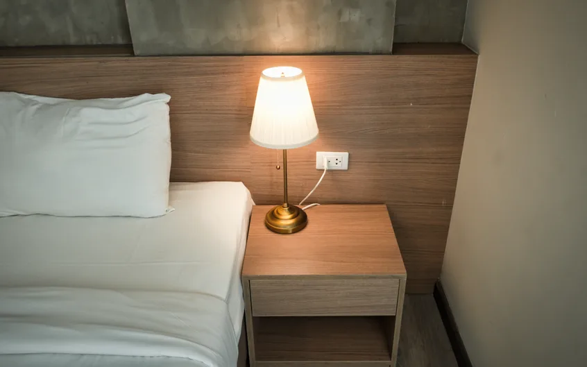 Chambre douce avec une lampe allumée sur une table de chevet en bois